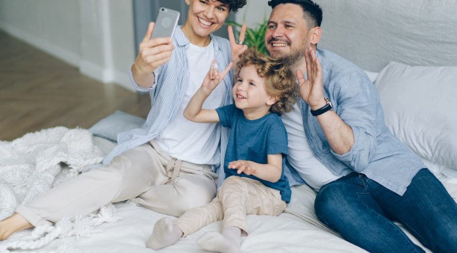 Mother father son taking selfie in bed at home posing for smartphone camera