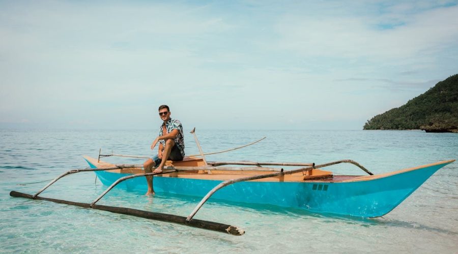 Relaxed man sitting on wooden vessel and relaxing against cloudy blue sky in sea